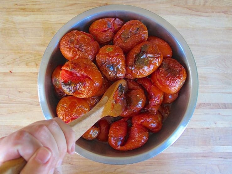 Crushing roasted tomatoes with a wooden spoon.