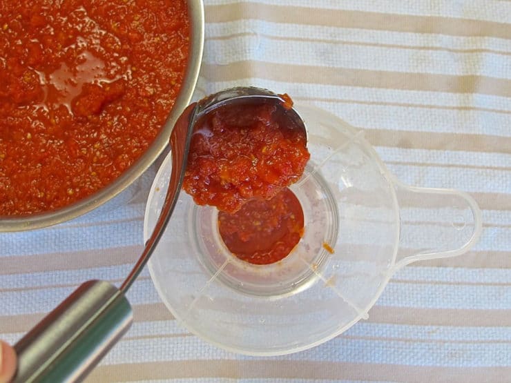 Using a wide mouth funnel to transfer tomato sauce into jars.