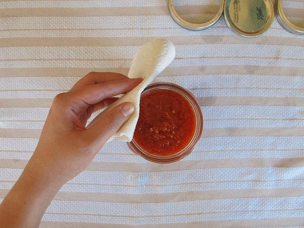 Cleaning the rims of canning jars with a towel.