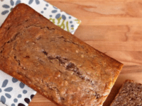 Banana Nut Bread on a wooden table with a towel on the side