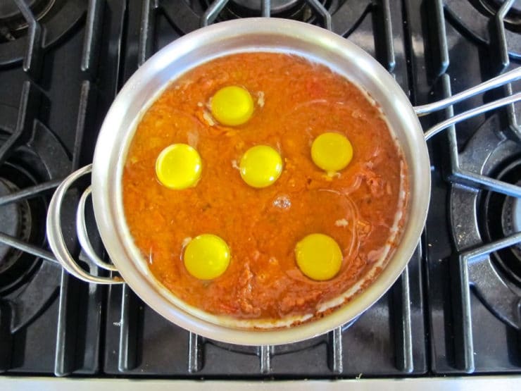 Eggs cracked into tomato sauce in pan.
