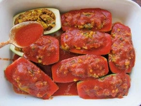 Tomato sauce spooned over stuffed zucchini in a baking dish.