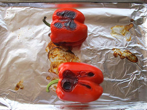 Red bell peppers roasting on a baking sheet.