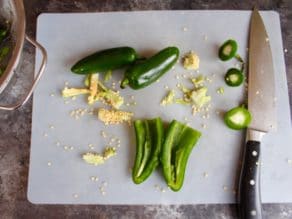 Jalapeno peppers sliced with seeds removed on cutting board on countertop with chef's knife