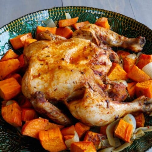 A close-up of Roasted Chicken elegantly presented on a round plate, surrounded by a colorful array of sliced vegetables, creating a visually appealing and appetizing dish.