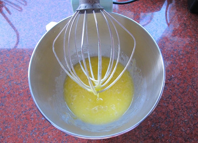 Beaten eggs on a huge mixing bowl that is attached to a mixer with stand