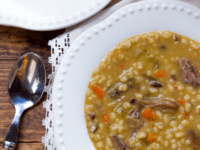 A comforting dish featuring beef flanken, mushrooms, and barley in a flavorful broth on a white plate with a spoon on the side