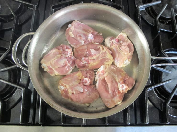 Chicken thighs searing in a pan.