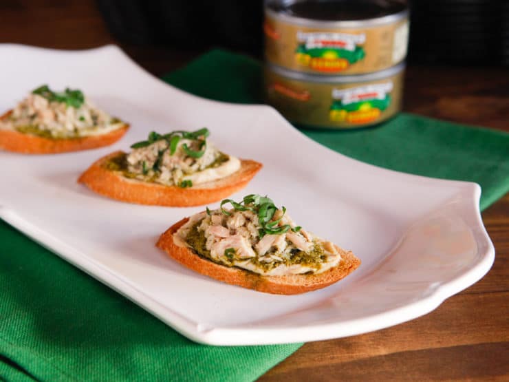 A horizontal cut image of Three Tuna, hummus, and pesto crostini appetizer served on a white plate