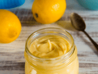 Lemon curd in a jar with lemons, a juicer, and a spoon on the side
