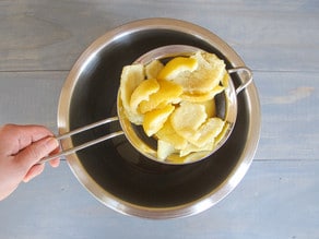 Lemon peels in mesh strainer over stainless steel bowl.