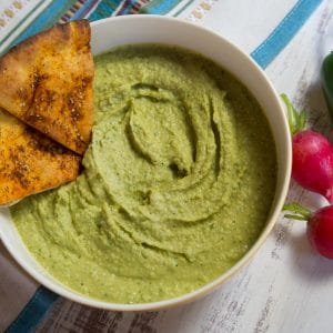 Green chile hummus with tortilla chips on a yellow bowl