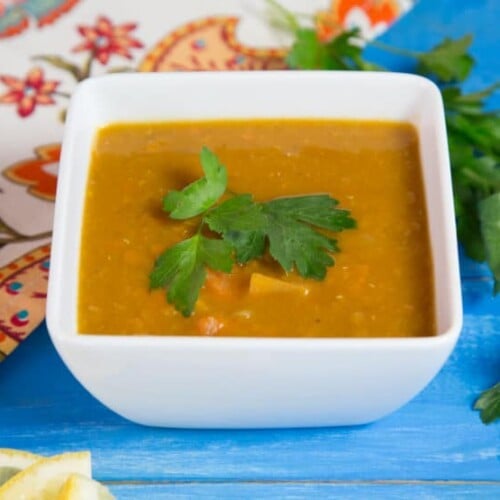 A bowl of smoky lentil sweet potato soup, garnished with fresh herbs