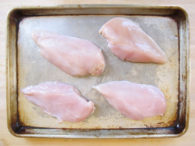 Trimmed chicken breasts on a baking sheet.