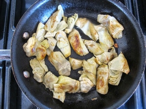 Browned artichoke hearts in a pan.