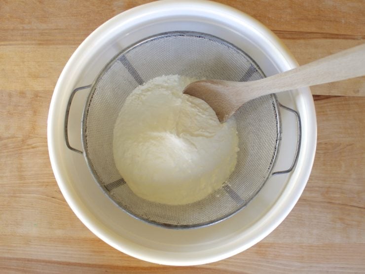 Wooden spoon mixing baking soda and citric acid through fine mesh strainer.