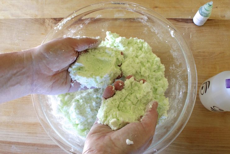 Dry ingredients tinted green, held in hands - sand-like texture.
