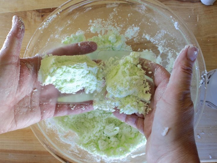 Hands shaping green-tinted bath fizzle mixture in mold.