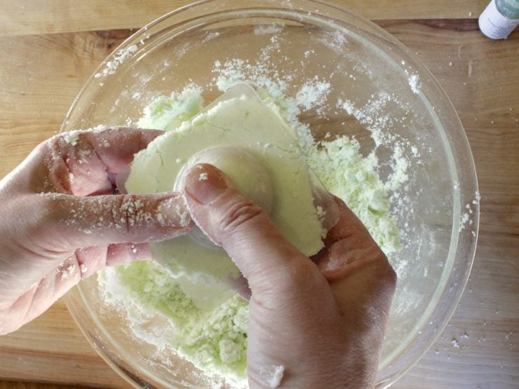 Hands lining up molds filled with green-tinted bath fizzle mixture.