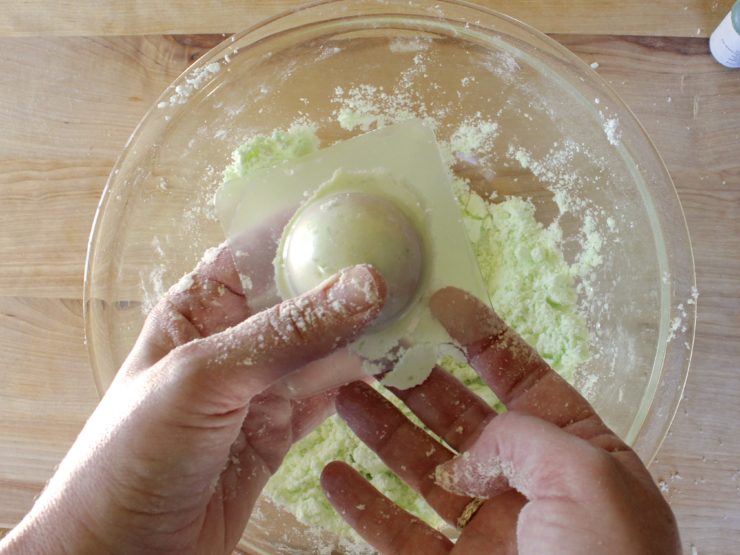 Fingers holding shaping green-tinted bath fizzle mixture in mold.