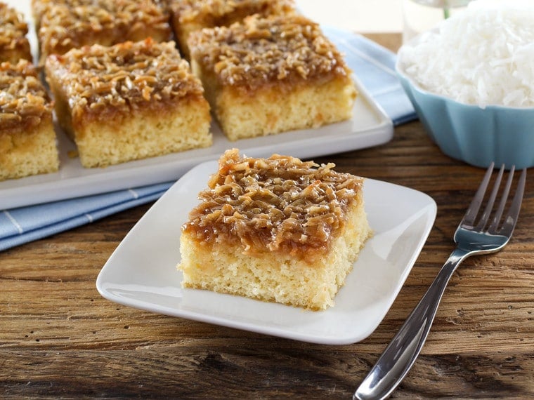 A plate full of square daisy flower cake slices, accompanied by a daisy flower in the background