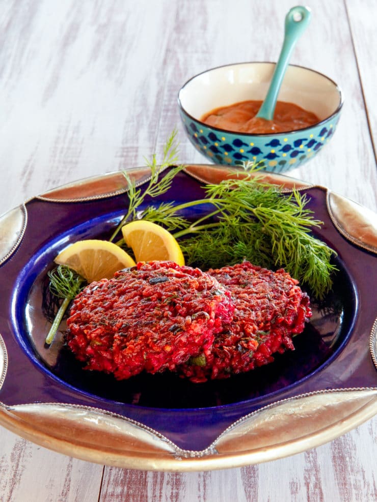 Close-up of The Red Rice and Beet Cake, a Crispy, fried vegetarian cake with a sweet Honey Mustard sauce served on a blue plate