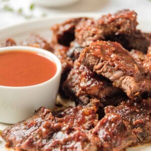 Close up horizontal shot - Vertical Crop- White plate of oven barbecued short ribs with sauce, garnished with fresh thyme, on a marble countertop.