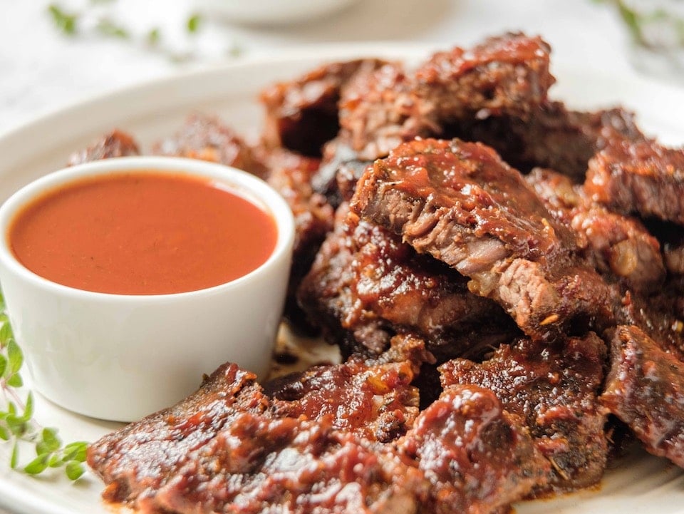 Close up horizontal shot - Vertical Crop- White plate of oven barbecued short ribs with sauce, garnished with fresh thyme, on a marble countertop.