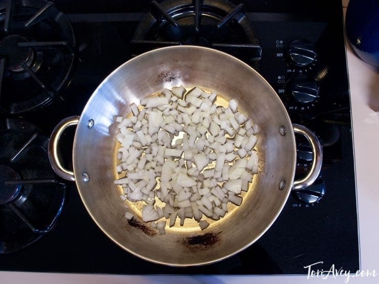 Onions cooking in pot on stovetop, overhead shot.