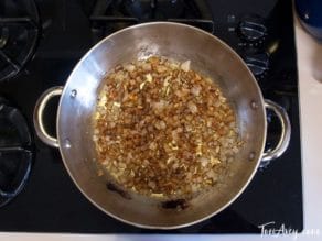 Onions and spices cooking in pot on stovetop, overhead shot.