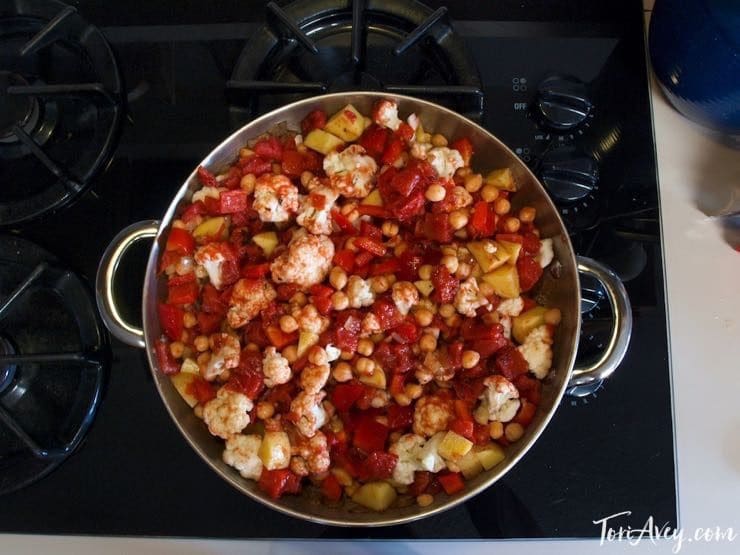 Cauliflower, tomatoes, chickpeas and spices cooking in pot on stovetop, overhead shot.