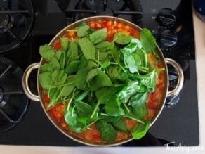 Curried Vegetable Stew cooking in pot on stovetop with fresh greens and coconut milk.