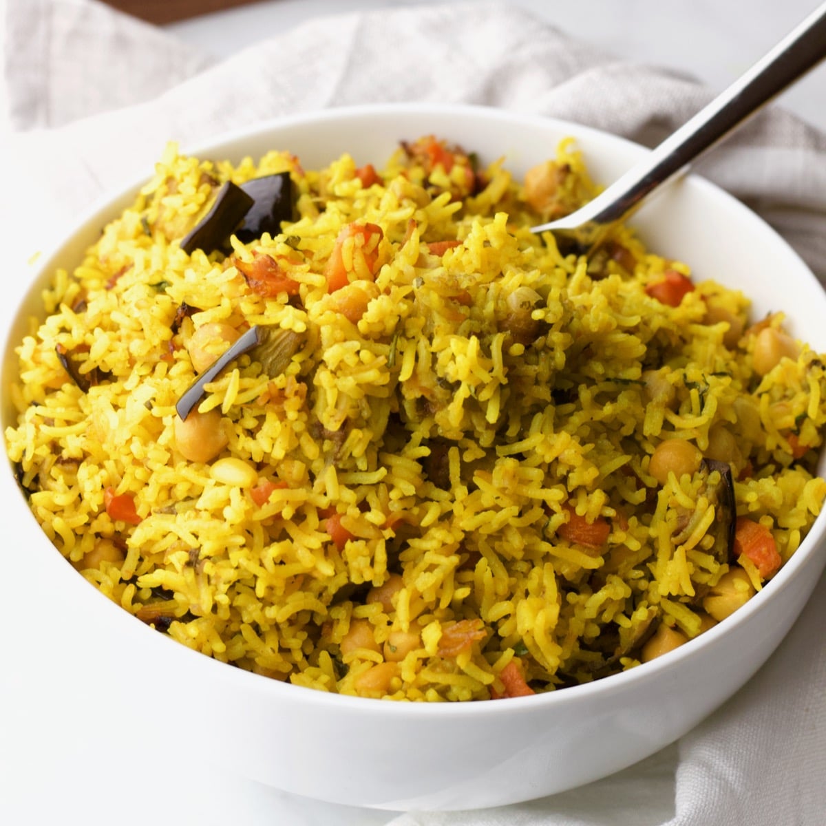 Vegetable rice in white bowl with spoon on white cloth background.