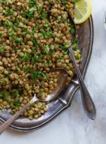 A plate of lentils topped with lemon wedges and parsley. A refreshing and nutritious Lentil Salad.