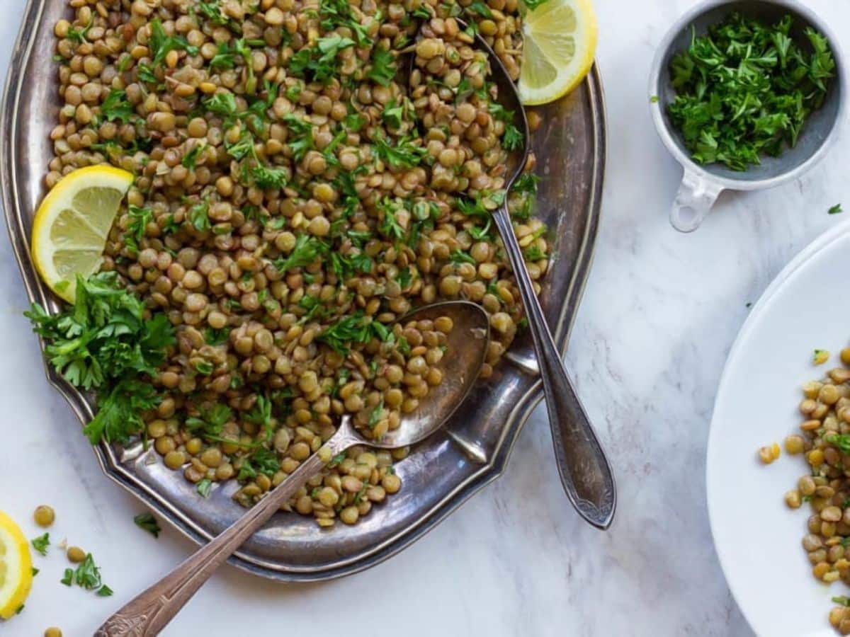 A plate of lentils topped with lemon wedges and parsley. A refreshing and nutritious Lentil Salad.
