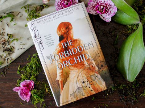 The Forbidden Orchid book on top of a wood table decorated with greens and orchid