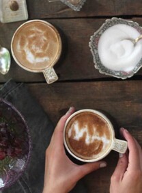 Two cups of coffee with latte art and a bowl of sugar on top of a wooden table
