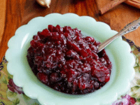 A bowl of vibrant red cranberry sauce with a spoon, made with orange blossom and cranberries on a white plate