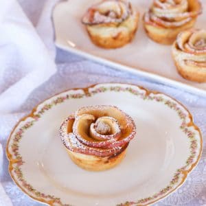 Apple Date Rose Tart served on a fancy white plate with floral designs and on top of a lace designed table clothe