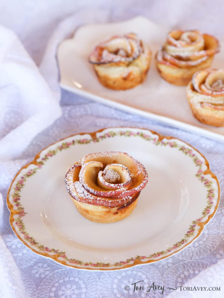 Apple Date Rose Tart served on a fancy white plate with floral designs and on top of a lace designed table clothe