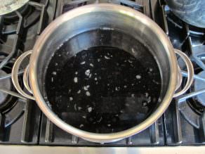 A pot of water simmering on a stove, containing dried black beans