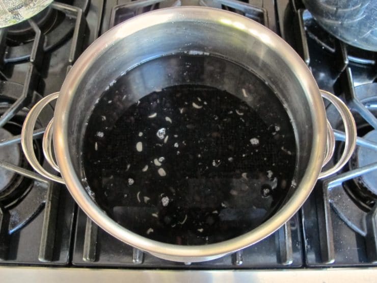 A pot of water simmering on a stove, containing dried black beans