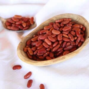 Horizontal shot - Wooden dish of dried Kidney Beans on a white cloth background, spoon of beans in background.