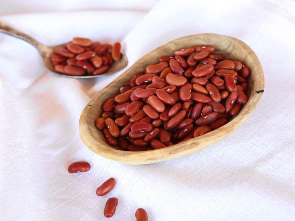Horizontal shot - Wooden dish of dried Kidney Beans on a white cloth background, spoon of beans in background.
