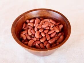 Wooden dish of cooked kidney beans on white background.