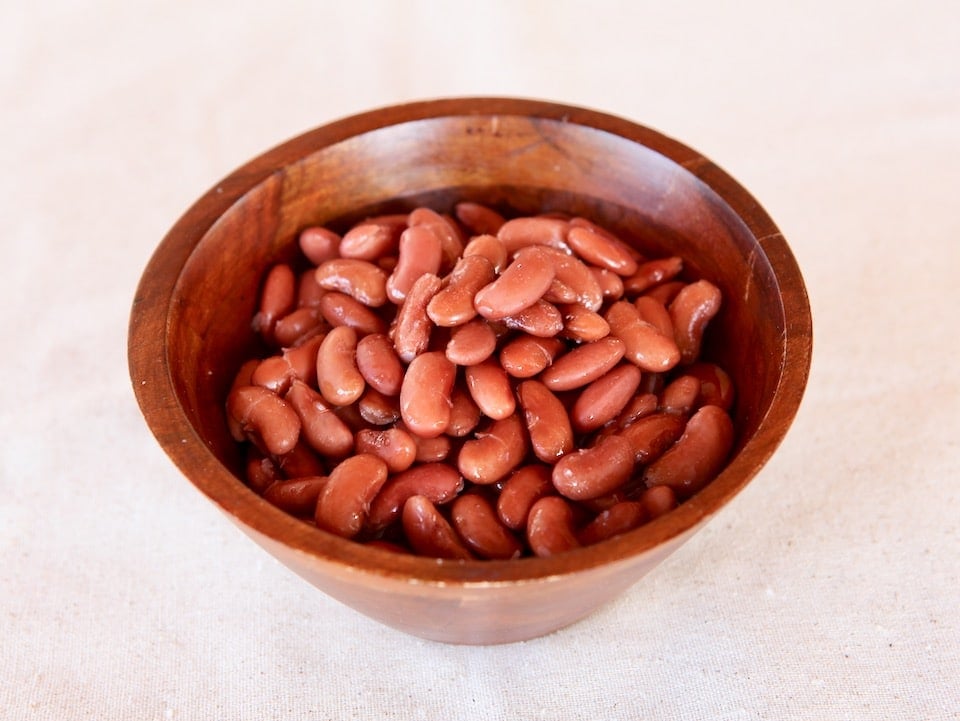 Wooden dish of cooked kidney beans on white background.