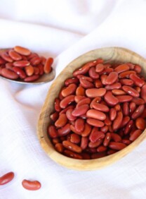 Square Crop - wooden dish of dried Kidney Beans on a white cloth background, spoon of beans in background.