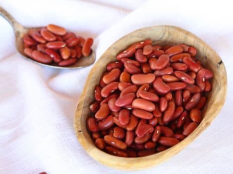 Square Crop - wooden dish of dried Kidney Beans on a white cloth background, spoon of beans in background.