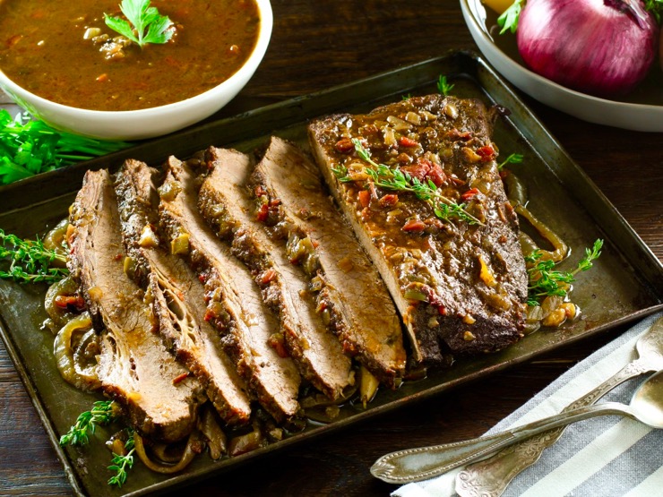 Overhead shot of West African Brisket on tray with bowl of sauce, topped with herbs.