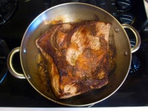 Brisket in pan on stovetop, seared brown.